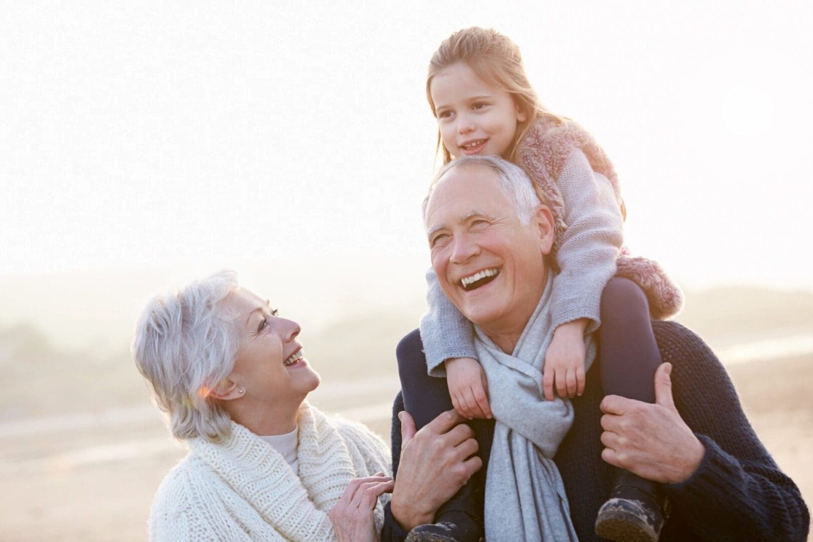 Happy elderly couple with a joyful child on the grandfather's shoulders outdoors.